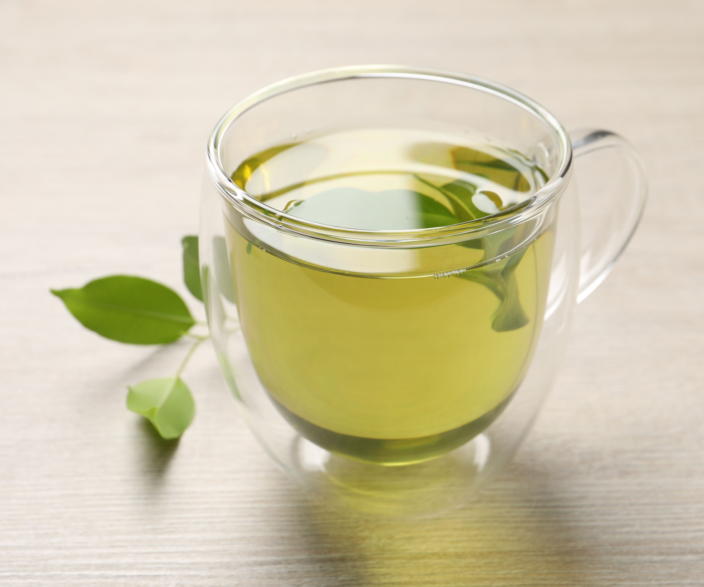 thé vert dans une tasse de thé en verre avec des feuilles sur le plan de travail
